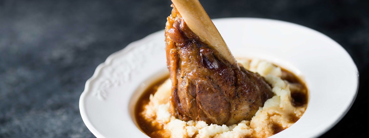 Front side angled view of lamb shanks on top of creamy mash and gravy in a bowl